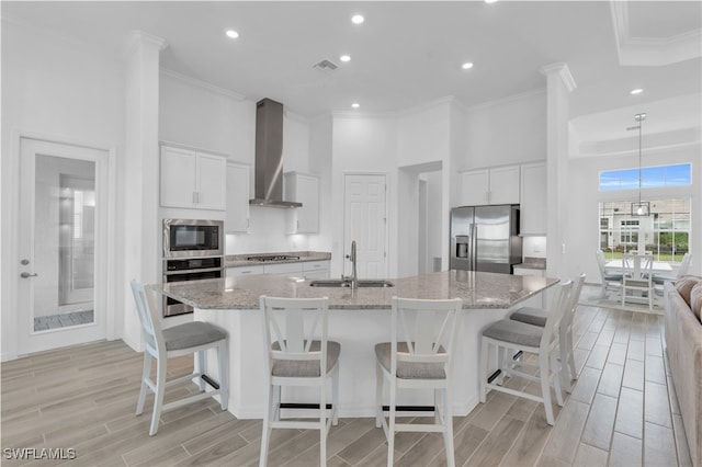 kitchen with wall chimney range hood, white cabinets, appliances with stainless steel finishes, and sink