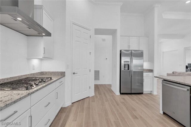 kitchen featuring white cabinets, crown molding, light wood-type flooring, appliances with stainless steel finishes, and wall chimney range hood