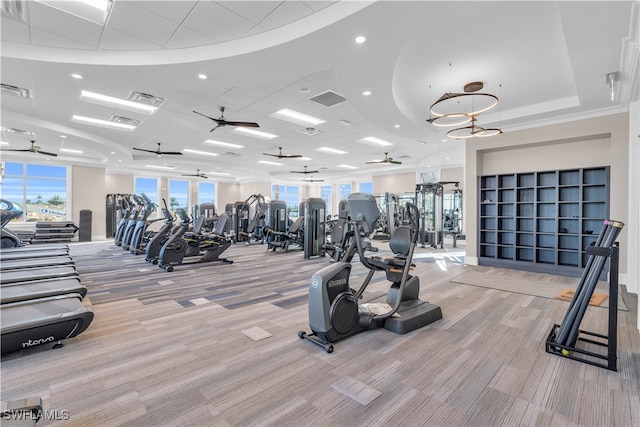 exercise room featuring ceiling fan, light carpet, and a tray ceiling