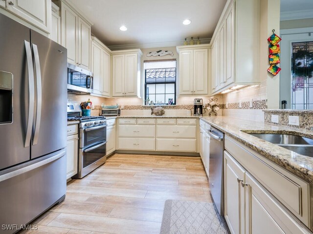 kitchen featuring light stone countertops, backsplash, cream cabinets, appliances with stainless steel finishes, and light wood-type flooring