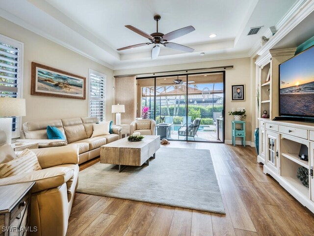 living room featuring a raised ceiling, crown molding, and light hardwood / wood-style flooring