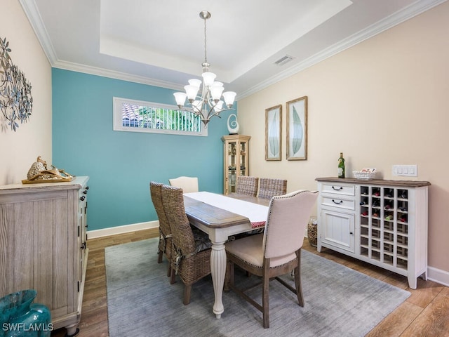 dining room with ornamental molding, hardwood / wood-style flooring, a raised ceiling, and a notable chandelier