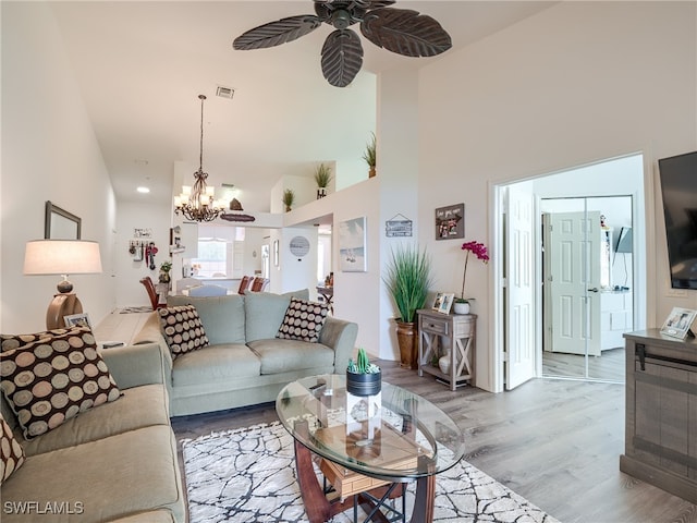 living room featuring a towering ceiling, ceiling fan with notable chandelier, and light hardwood / wood-style floors