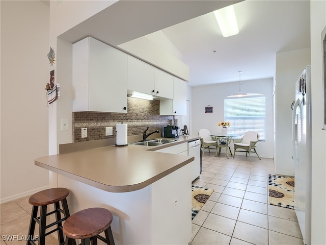 kitchen with white appliances, decorative light fixtures, kitchen peninsula, sink, and a breakfast bar area