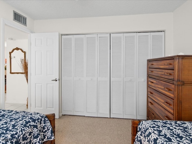 bedroom with a textured ceiling, light colored carpet, and a closet