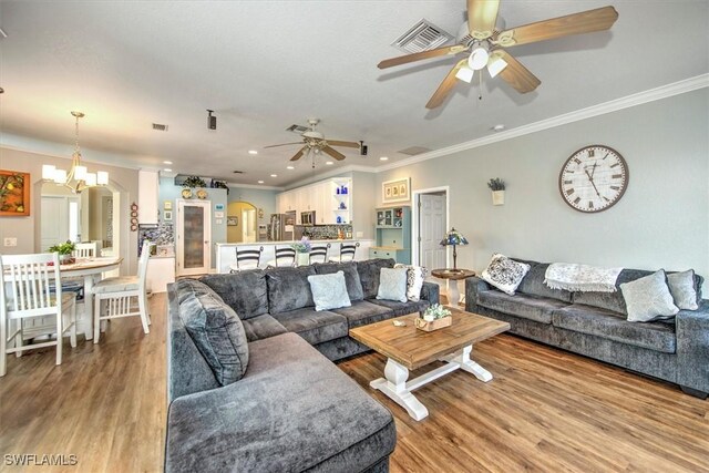 living room with ceiling fan with notable chandelier, light hardwood / wood-style floors, and crown molding