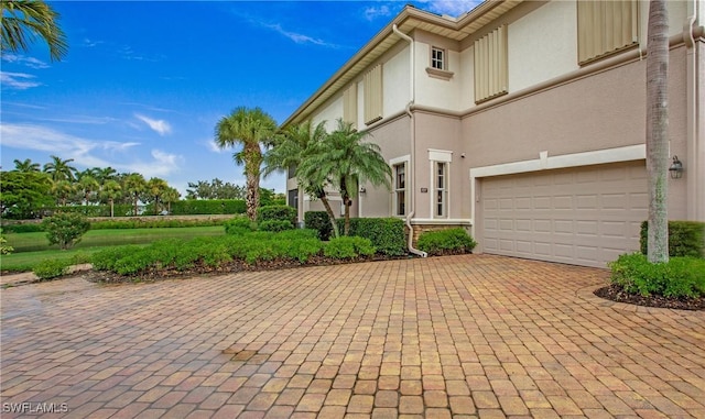 view of front of home featuring an attached garage, decorative driveway, and stucco siding