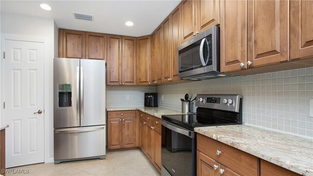 kitchen featuring light tile patterned floors, stainless steel appliances, light stone countertops, and decorative backsplash