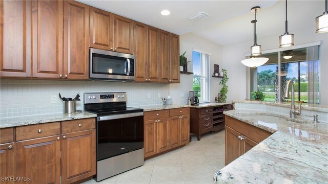 kitchen with appliances with stainless steel finishes, brown cabinetry, a sink, and light stone counters