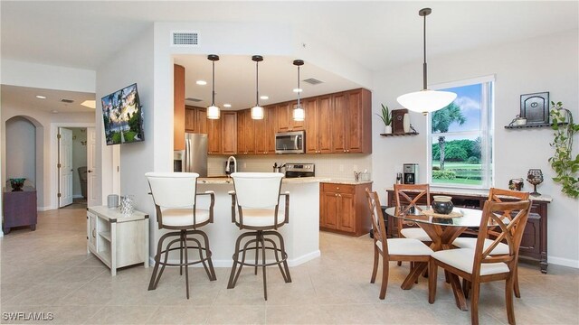 kitchen featuring decorative light fixtures, appliances with stainless steel finishes, a kitchen bar, decorative backsplash, and light tile patterned flooring