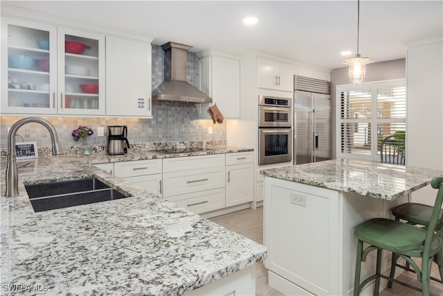 kitchen featuring white cabinetry, pendant lighting, stainless steel appliances, sink, and wall chimney range hood