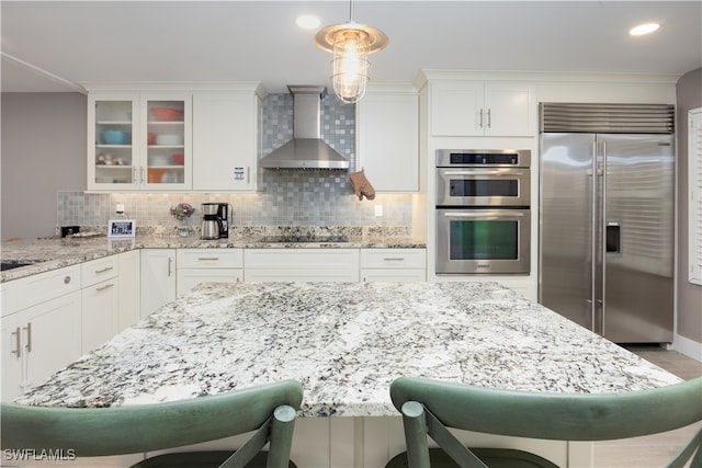 kitchen with white cabinetry, a breakfast bar, wall chimney exhaust hood, stainless steel appliances, and decorative light fixtures