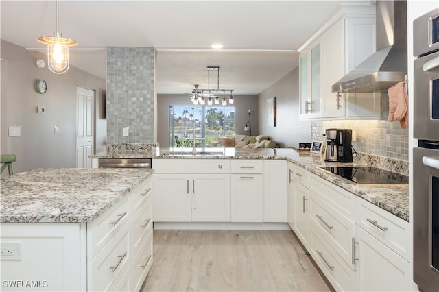 kitchen with kitchen peninsula, decorative light fixtures, wall chimney exhaust hood, white cabinetry, and appliances with stainless steel finishes