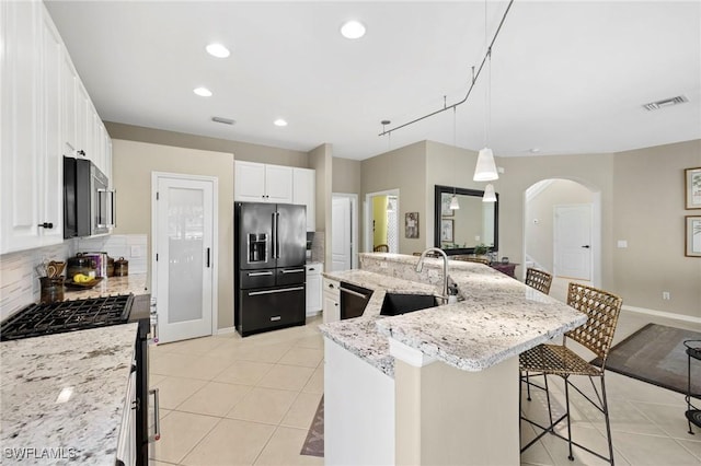 kitchen featuring a sink, light tile patterned floors, black appliances, backsplash, and arched walkways