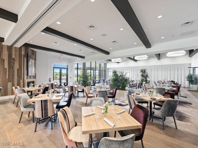 dining space with light hardwood / wood-style flooring, wood walls, and beamed ceiling