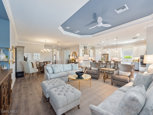 living room with ornamental molding, ceiling fan with notable chandelier, a raised ceiling, and hardwood / wood-style floors