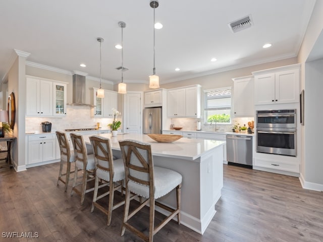 kitchen featuring white cabinetry, a center island, wall chimney range hood, and stainless steel appliances