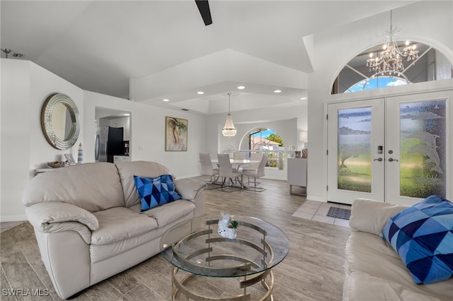 living room with lofted ceiling, french doors, an inviting chandelier, and light hardwood / wood-style flooring