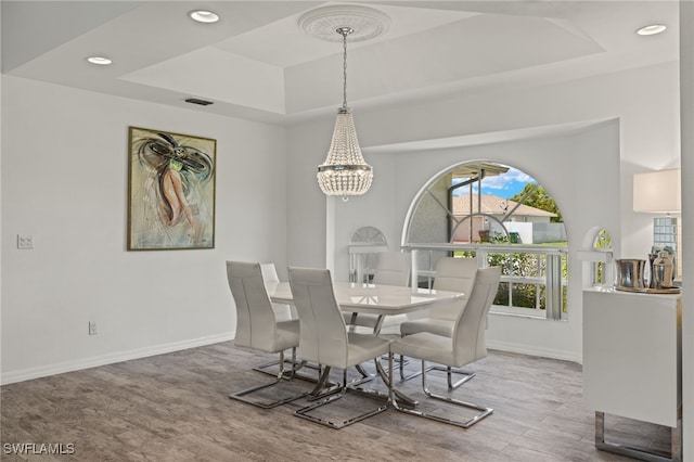 dining space featuring light wood-type flooring, an inviting chandelier, and a raised ceiling