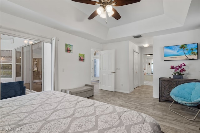 bedroom featuring ensuite bath, a raised ceiling, ceiling fan, and light hardwood / wood-style floors