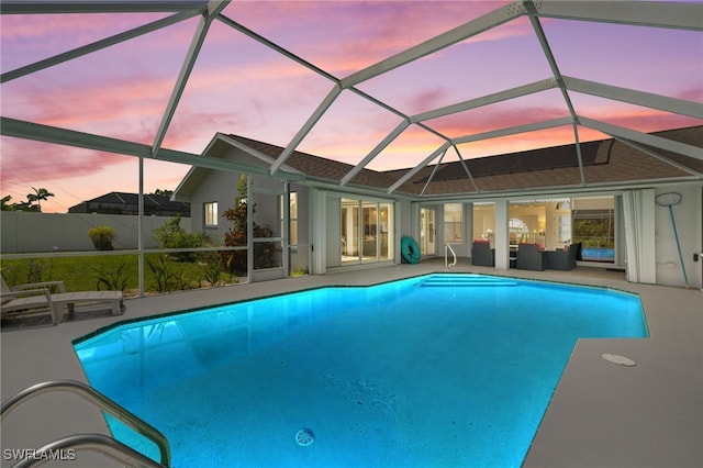 pool at dusk with glass enclosure and a patio area