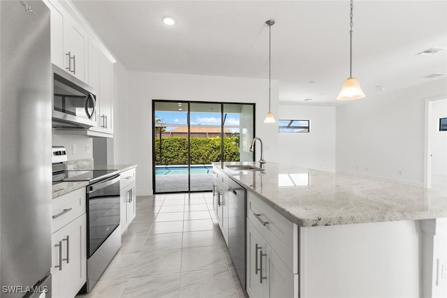 kitchen with pendant lighting, sink, white cabinets, stainless steel appliances, and a center island with sink