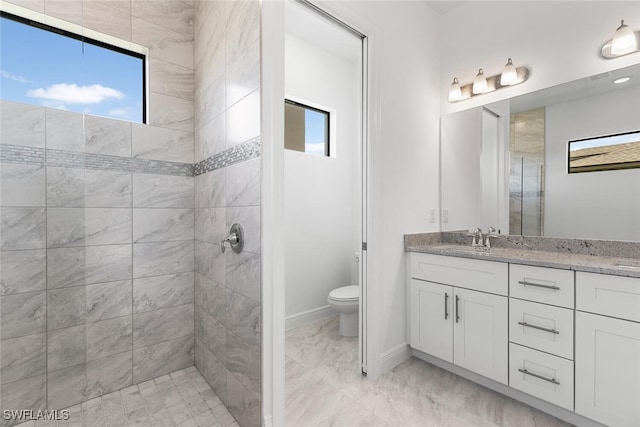 bathroom featuring a tile shower, vanity, and toilet