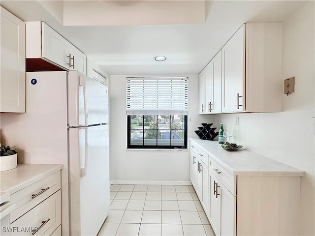 kitchen with light countertops, light tile patterned flooring, freestanding refrigerator, and white cabinetry