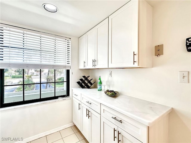 kitchen featuring baseboards, white cabinetry, light stone counters, and light tile patterned flooring