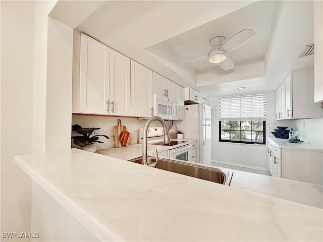 kitchen featuring light countertops, white appliances, a raised ceiling, and white cabinetry