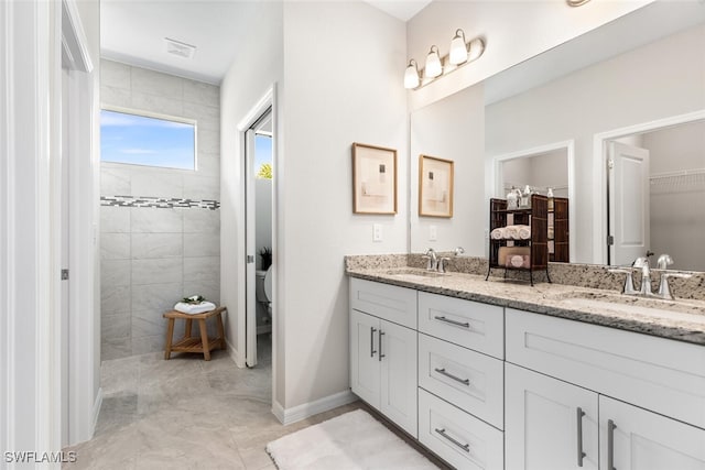 bathroom featuring double vanity, a sink, baseboards, and walk in shower