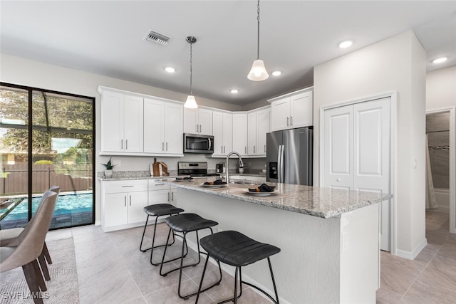 kitchen with a healthy amount of sunlight, stainless steel appliances, white cabinets, and a center island with sink