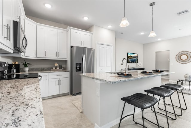 kitchen with stainless steel appliances, sink, light stone countertops, a center island with sink, and white cabinets