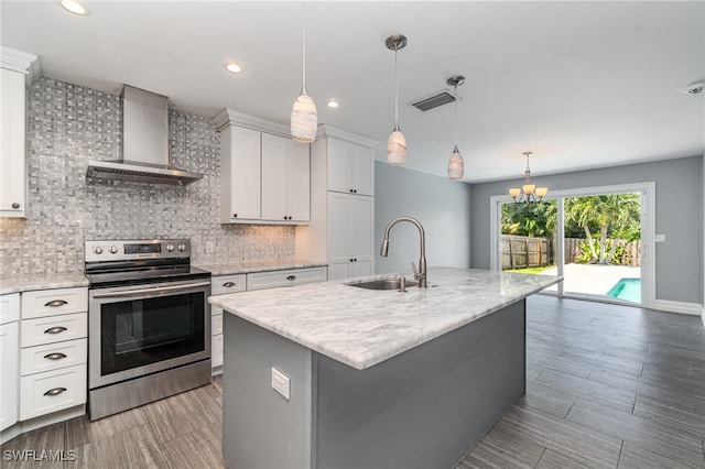 kitchen with wall chimney exhaust hood, a kitchen island with sink, sink, white cabinets, and stainless steel range with electric cooktop