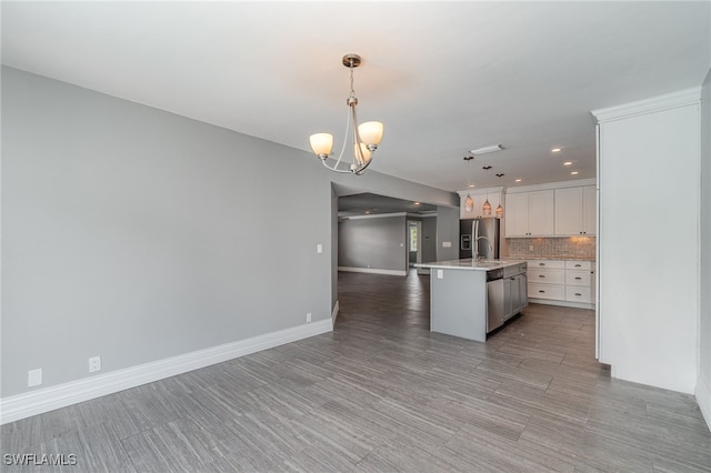 kitchen featuring backsplash, light hardwood / wood-style floors, white cabinetry, an island with sink, and pendant lighting