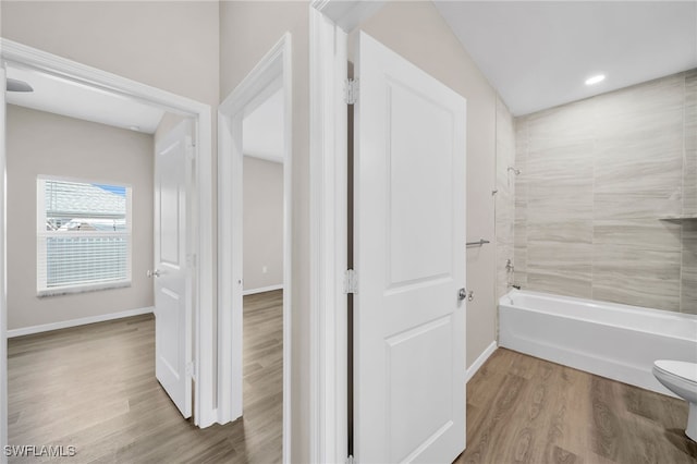 bathroom with lofted ceiling, toilet, tiled shower / bath combo, and hardwood / wood-style floors