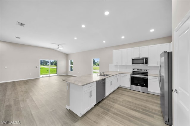 kitchen with vaulted ceiling, light hardwood / wood-style flooring, stainless steel appliances, sink, and kitchen peninsula