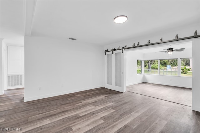 empty room featuring ceiling fan, hardwood / wood-style flooring, and a barn door