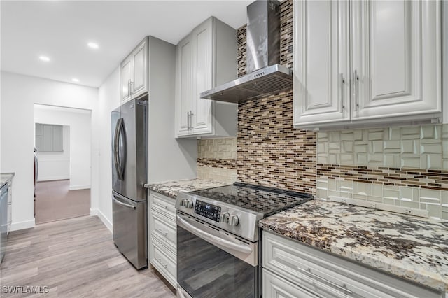 kitchen with light stone counters, wall chimney exhaust hood, white cabinetry, stainless steel appliances, and light wood-type flooring