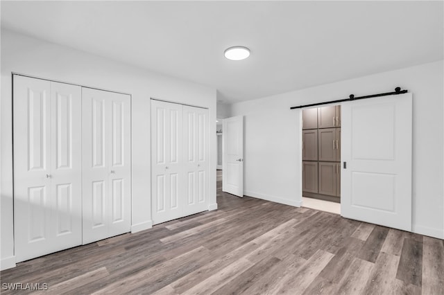 unfurnished bedroom featuring a barn door, light hardwood / wood-style flooring, and two closets