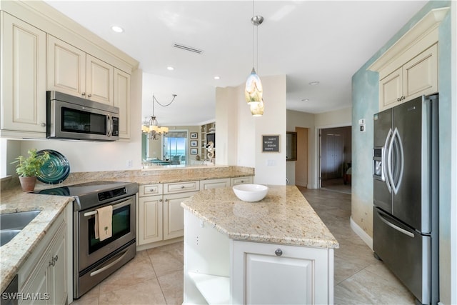 kitchen with appliances with stainless steel finishes, light stone counters, a kitchen island, pendant lighting, and cream cabinets