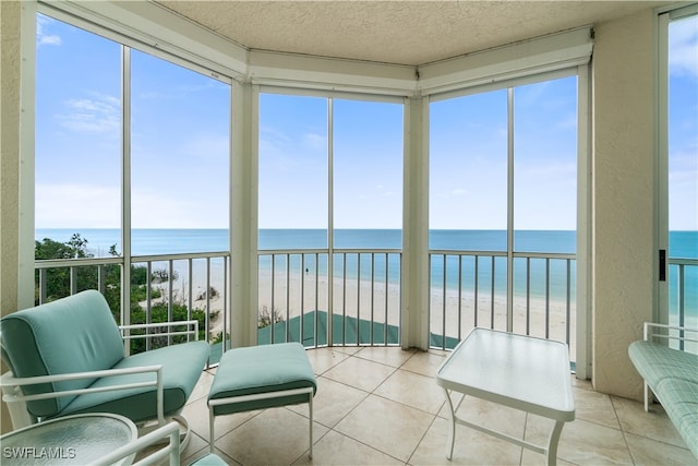 sunroom / solarium featuring a beach view, plenty of natural light, and a water view