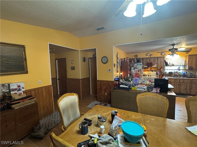 dining area featuring hardwood / wood-style floors, ceiling fan, a textured ceiling, wood walls, and sink