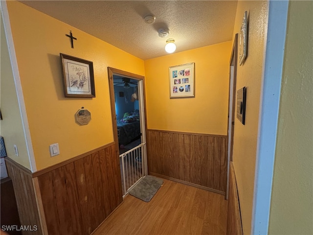 corridor featuring a textured ceiling, light wood-type flooring, and wood walls