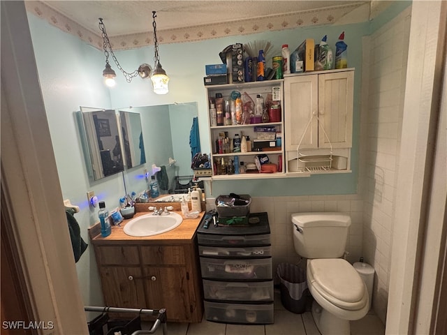 bathroom featuring a textured ceiling, toilet, tile walls, vanity, and tile patterned flooring