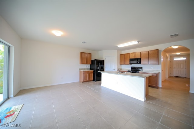 kitchen featuring an island with sink, black appliances, light tile patterned floors, and sink