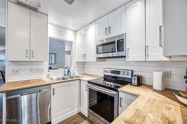 kitchen with butcher block countertops, white cabinets, appliances with stainless steel finishes, and sink