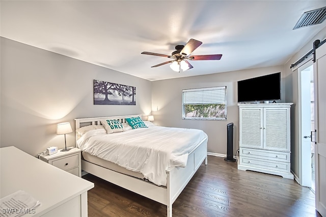 bedroom featuring ceiling fan, a barn door, and dark hardwood / wood-style floors