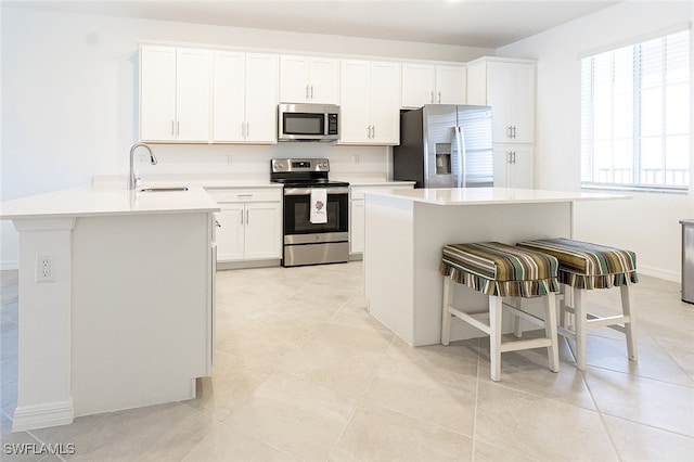 kitchen with sink, an island with sink, stainless steel appliances, and white cabinetry