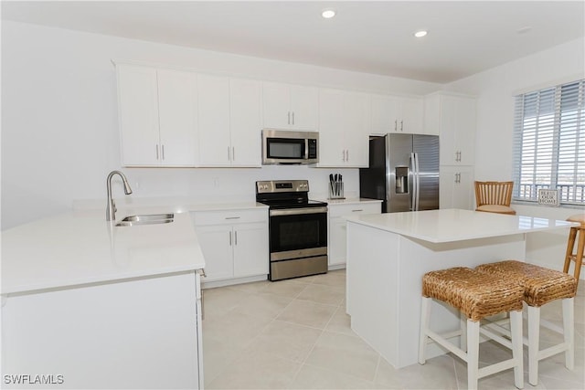 kitchen featuring white cabinets, stainless steel appliances, sink, a breakfast bar, and light tile patterned floors